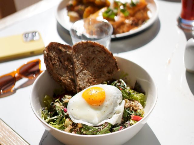 A bowl with a salad topped with a fried egg and bread slices on the side, with another dish and items on the table.