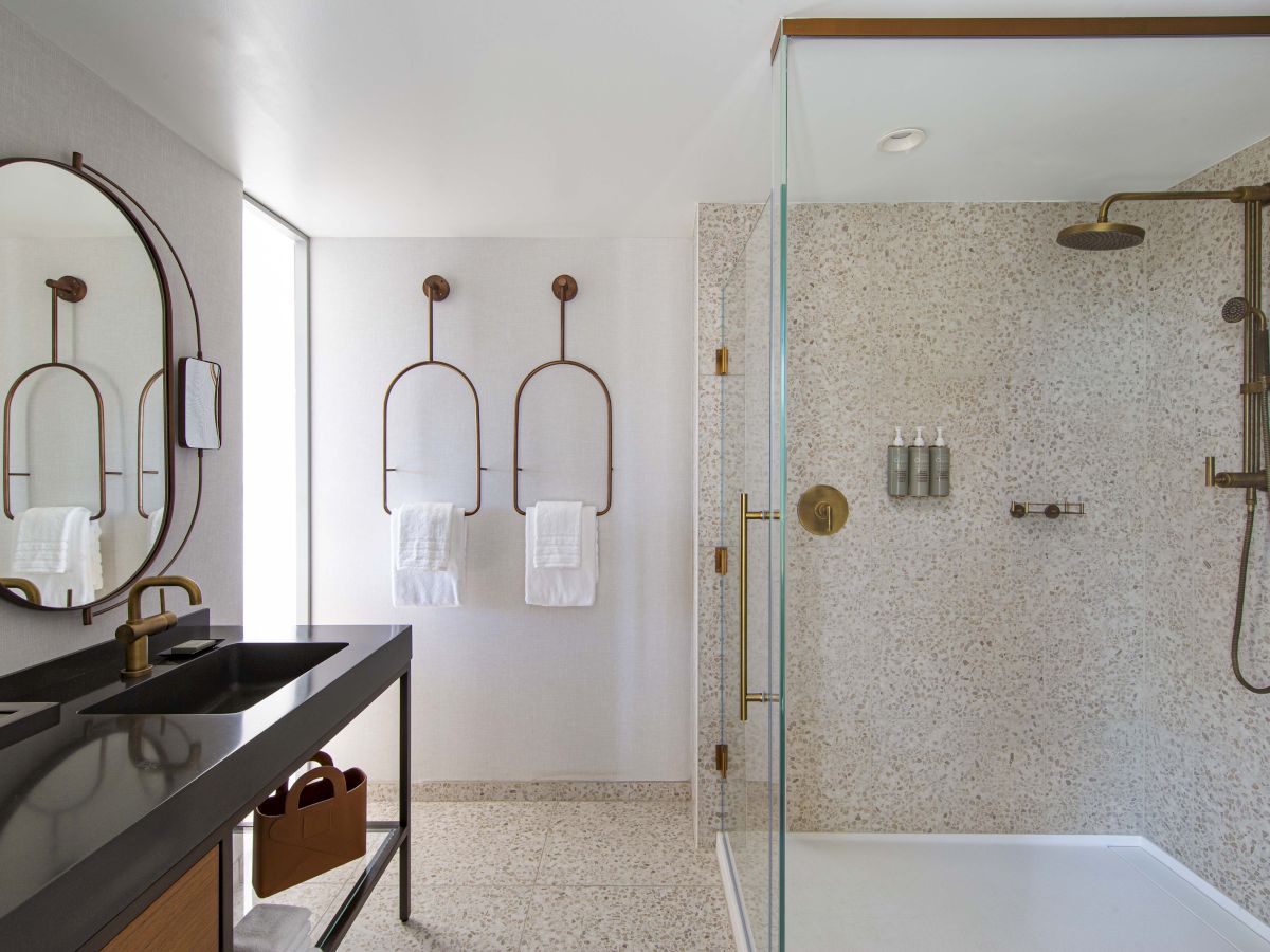 A modern bathroom features a black sink, two circular towel racks, and a glass-enclosed shower with brass fixtures and toiletries.