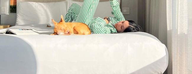 A person in green striped pajamas lies on a bed with a small dog sleeping beside them, enjoying a relaxed moment.